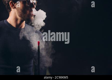 Attraktiver Mann, der Rauch aus der Nase ausatmet. Nahaufnahme Seitenansicht shot.man in einer Brille, die eine Shisha anwirbt Stockfoto