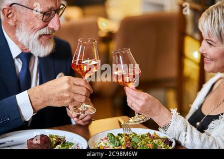 Schöne ältere Pärchen haben eine Mahlzeit in sympathisches Restaurant, verliebt. Grauhaarige männliche und weibliche Getränke- und Klappgläser mit Champagner. Stockfoto