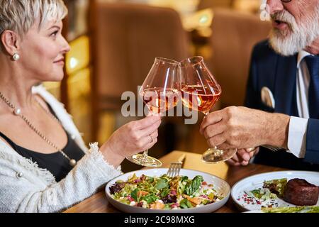 Schöne ältere Pärchen haben eine Mahlzeit in sympathisches Restaurant, verliebt. Grauhaarige männliche und weibliche Getränke- und Klappgläser mit Champagner. Stockfoto