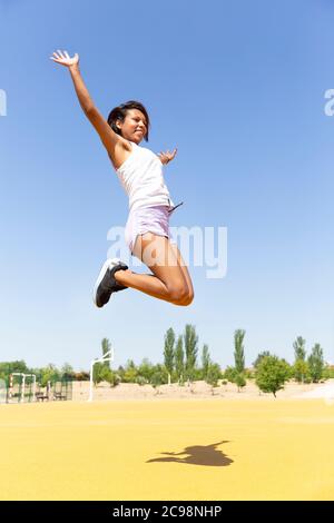 Junge Frau in einem Tank-Top und Shorts springen energisch auf der Sportarena. Stockfoto