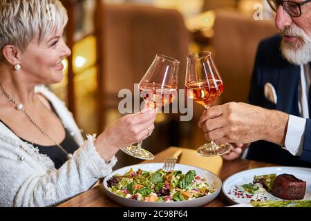 Schöne ältere Pärchen haben eine Mahlzeit in sympathisches Restaurant, verliebt. Grauhaarige männliche und weibliche Getränke- und Klappgläser mit Champagner. Stockfoto