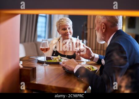 Ältere hübsche Frau und reifer Mann in Smoking sprechen und schauen sich gegenseitig, romantische Datum im Restaurant. Feuer vom Kamin. Horizontales Bild Stockfoto