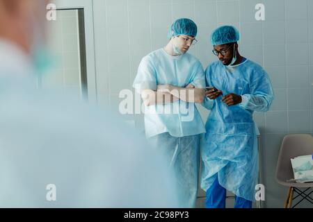 Serious attraktive Ärzte reden und mit Smartphone während der Arbeit. Nahaufnahme Foto. Gadget Konzept. afro junger Mann im Netz surfen , zeigt Informationen Stockfoto