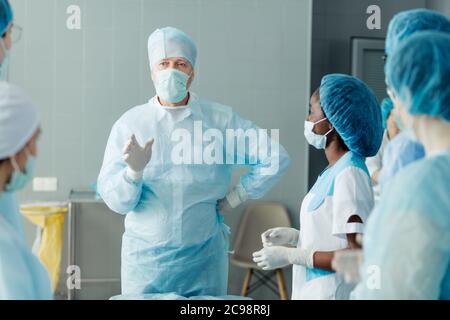 Clever Chirurg mit der Hand an der Hüfte erklärt das Detail der Operation. Attraktive alte Arzt Beratung seiner gemischten Rennen Kollegen Stockfoto