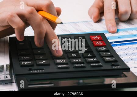 Taschenrechner und Hände mit Bleistift. Desktop mit Finanz- und Buchhaltungsunterlagen. Person zählt auf einen Rechner und analysiert die Daten. Stockfoto