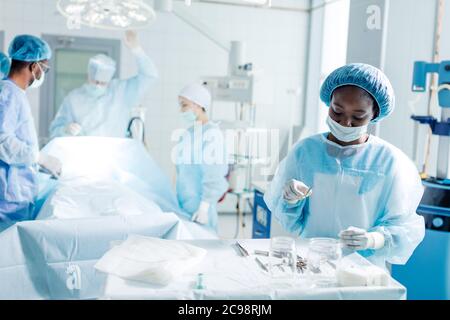 Gut aussehende fröhliche Krankenschwester mit steralisierten medizinischen Instrument konzentriert auf die Arbeit. Nahaufnahme Foto. Menschen im Hintergrund des Fotos Stockfoto