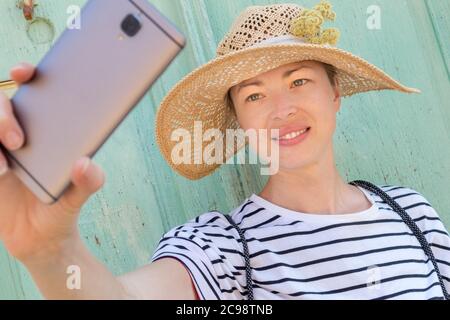 Schöne junge Frau Touristen tragen großen Strohhut, Selbstporträt Selfie, stehen vor vinatage türkis Holztür bei alt Stockfoto