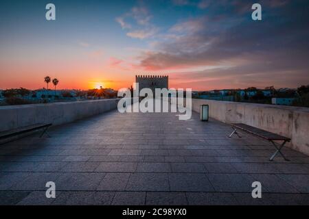 Sonnenaufgang in der spanischen Stadt Cordoba mit dramatischen Morgenwolken. Historische römische Brücke in der Altstadt. Brückenturm mit Fußweg über den Fluss Stockfoto