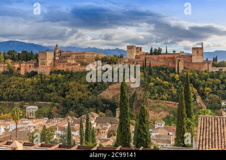 Spanische Stadt Granada in Andalusien mit Wolken und Bergen im Hintergrund. Historische Alhambra Festung mit Bäumen und Gebäuden auf einem Hügel. Stockfoto