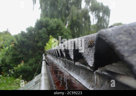 Regen strömt während eines Regenschauens vom gekräuselten Dach in eine Rinne. Stockfoto