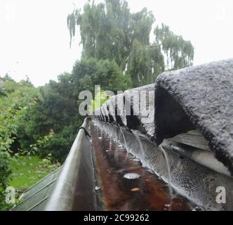 Regen strömt während eines Regenschauens vom gekräuselten Dach in eine Rinne. Stockfoto