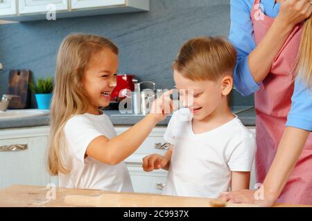 Junge blonde Frau, Mutter und ihre Kinder haben Spaß beim Kochen Teig Stockfoto