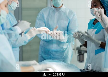 Müde gemischte Rennen Ärzte Ausziehen Handschuhe nach erfolgreicher Operation. Close up beschnitten Foto.Focus auf Latex-Handschuhe Stockfoto