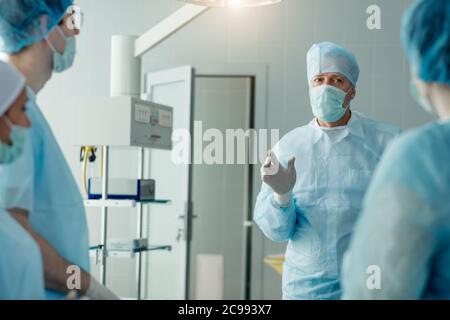 Schöner alter Chirurg, der seinen Praktikanten Ratschläge gibt. Mann, der mit Informationen in der Klinik teilt Stockfoto