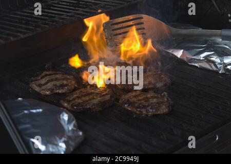 Eine Person, die Burger auf dem Grill mit Flammen dreht Stockfoto