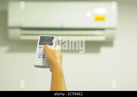 Frau, die die Fernbedienung bediente. / Klimaanlage mit Fernbedienung Stockfoto
