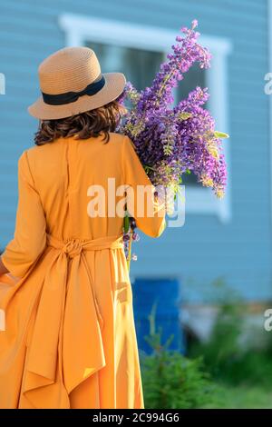 Mädchen in einem Strohhut halten einen Strauß Lupine in ihren Händen. Rückansicht. Stockfoto