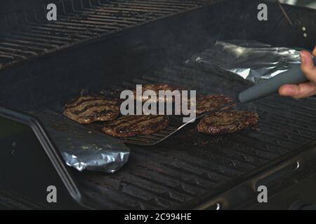 Eine Person, die Burger auf dem Grill mit Flammen dreht Stockfoto