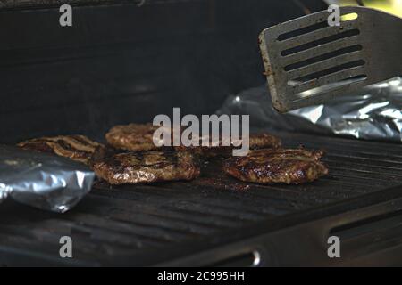 Eine Person, die Burger auf dem Grill mit Flammen dreht Stockfoto