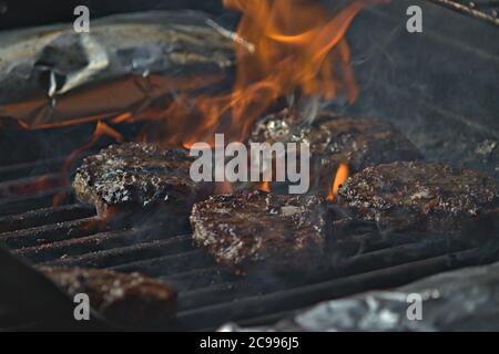 Eine Person, die Burger auf dem Grill mit Flammen dreht Stockfoto