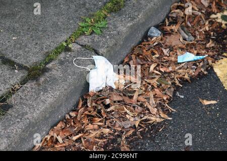 Eine Einweg-Gesichtsmask liegt auf der Straße weggeworfen Müll an der Bordwand, Großbritannien, Juli 2020 Stockfoto