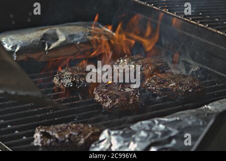 Eine Person, die Burger auf dem Grill mit Flammen dreht Stockfoto