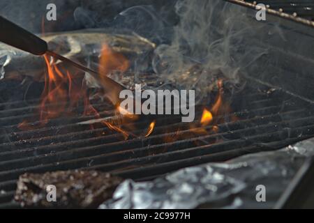 Eine Person, die Burger auf dem Grill mit Flammen dreht Stockfoto