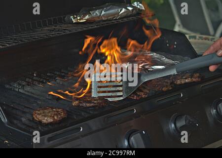 Eine Person, die Burger auf dem Grill mit Flammen dreht Stockfoto