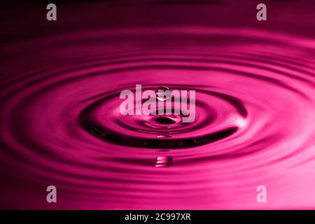 Perfekter Wassertropfen, der in glattes Wasser spritzt und Wellen verursacht Eine rosa Farbe Stockfoto