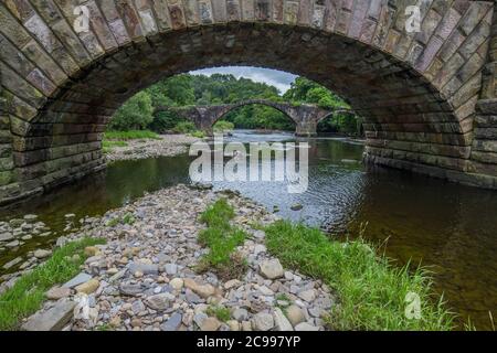 Cromwells Brücke im Ribble Valley, Lancashire. Alte Steinbrücke über den Fluss Hodder schoss durch einen Bogen der neueren unteren Hodderbrücke. Stockfoto