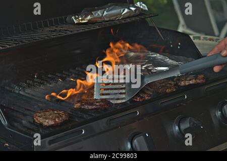 Eine Person, die Burger auf dem Grill mit Flammen dreht Stockfoto