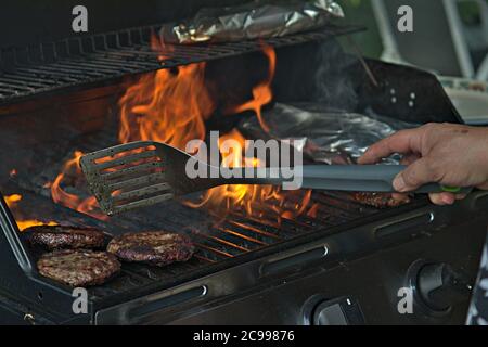 Eine Person, die Burger auf dem Grill mit Flammen dreht Stockfoto