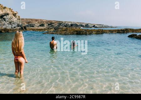 Junge Leute betreten das kalte Wasser am Strand Praia dos Buizinhos in Porto Covo, Alentejo, Portugal Stockfoto