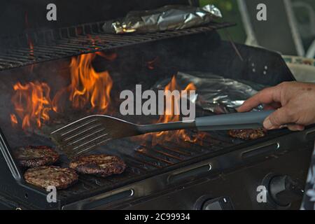 Eine Person, die Burger auf dem Grill mit Flammen dreht Stockfoto