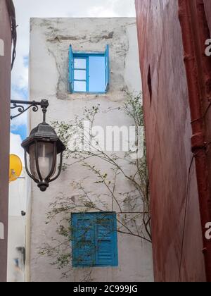 Weiße und rosa Wände mit blauen Fenstern und einer Laterne in Asilah Medina, Marokko. Stockfoto