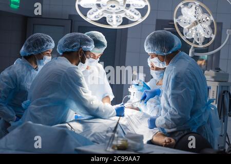 Gruppe von Zusammengeschlossenen Chirurgen engagieren in die Rettung von männlichen Patienten in Betrieb Zimmer im Krankenhaus, Notfall, Chirurgie, Medizintechnik, Gesundheit c Stockfoto