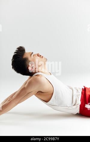 Asiatische Straßentänzerin in roten Sporthosen, die sich vor dem Training im weißen Studio aufwärmen. Stockfoto