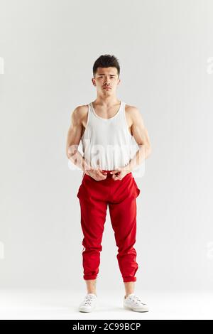Asiatische Straßentänzerin in roten Sporthosen posiert vor dem Training im weißen Studio vor der Kamera. Stockfoto