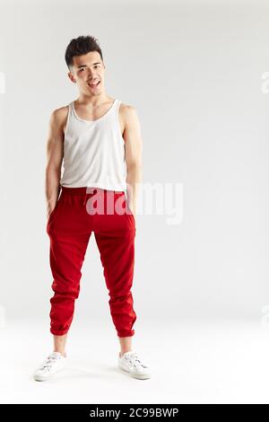 Junge sportliche stilvolle männliche Tänzerin in roten Jogginghosen posiert isoliert im Studio über weißem Hintergrund. Asiatische Hipster bboy lächelnd bei Kamera vor traini Stockfoto
