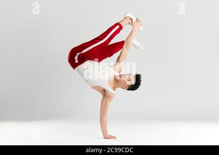 Junge koreanische männliche Tänzerin, die grundlegende Einfrierungen von Downrock Break ausführt, zeigt die Tanzbewegungen des zeitgenössischen Tanzes in sportlichen roten Trainingshosen für den Sport Stockfoto