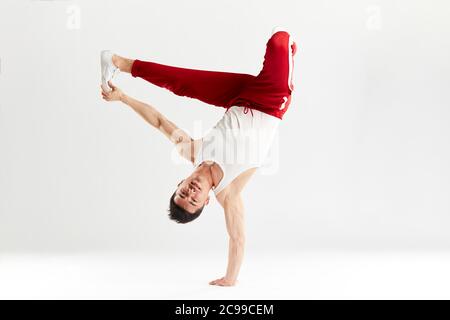 Junge koreanische männliche Tänzerin, die grundlegende Einfrierungen von Downrock Break ausführt, zeigt die Tanzbewegungen des zeitgenössischen Tanzes in sportlichen roten Trainingshosen für den Sport Stockfoto