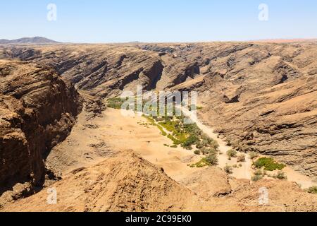 Typisch trostlose, aride geschichtete Felsen bergiges Gelände und ausgetrocknetes Flussbett in der Namib Wüste an der Skeleton Küste, Namibia, Südwestafrika Stockfoto