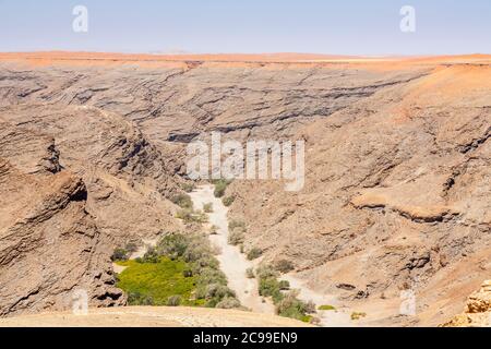 Typisch trostlose, aride geschichtete Felsen bergiges Gelände und ausgetrocknetes Flussbett in der Namib Wüste an der Skeleton Küste, Namibia, Südwestafrika Stockfoto