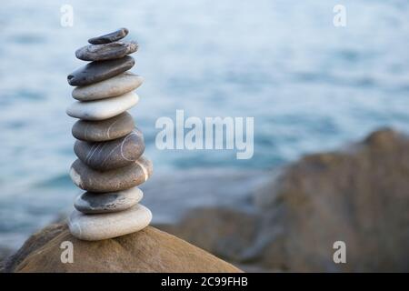 Steinpyramide auf Sand symbolisiert Zen, Harmonie, Gleichgewicht. Ozean bei Sonnenuntergang im Hintergrund. Stockfoto