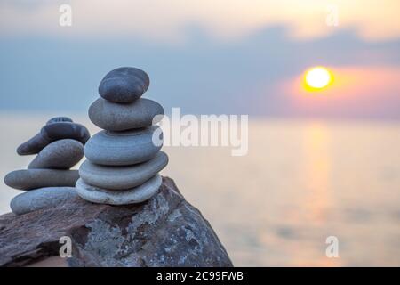 Steinpyramide auf Sand symbolisiert Zen, Harmonie, Gleichgewicht. Ozean bei Sonnenuntergang im Hintergrund. Stockfoto