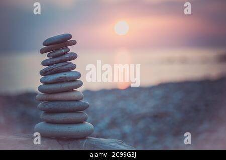 Steinpyramide auf Sand symbolisiert Zen, Harmonie, Gleichgewicht. Ozean bei Sonnenuntergang im Hintergrund. Stockfoto