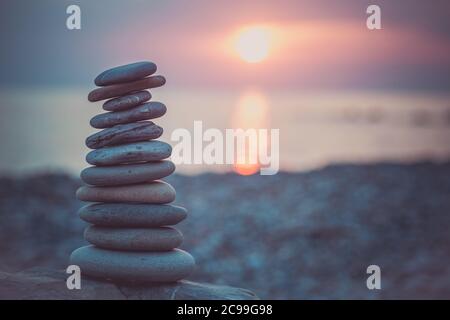 Steinpyramide auf Sand symbolisiert Zen, Harmonie, Gleichgewicht. Ozean bei Sonnenuntergang im Hintergrund. Stockfoto