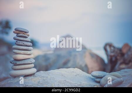 Steinpyramide auf Sand symbolisiert Zen, Harmonie, Gleichgewicht. Ozean bei Sonnenuntergang im Hintergrund. Stockfoto