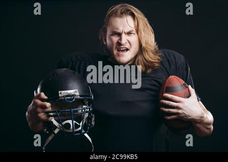 Wütend american Football Trainer hält Fußball über isolierten Hintergrund, bereit, um den Sieg zu kämpfen, schreien vor Wut und Aufregung, Sport und EM Stockfoto