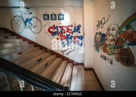 Chongqing, China - August 2019 : Wand Graffiti Darstellung des Menschen auf einem großen Fahrrad, bunte Schrift und große Buddha Kopf innerhalb Wohn b gemalt Stockfoto